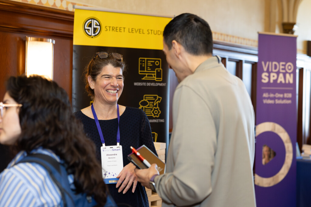 Photo of a 2025 BrandSmart attendee talking with a sponsor at their booth. Both are smiling.